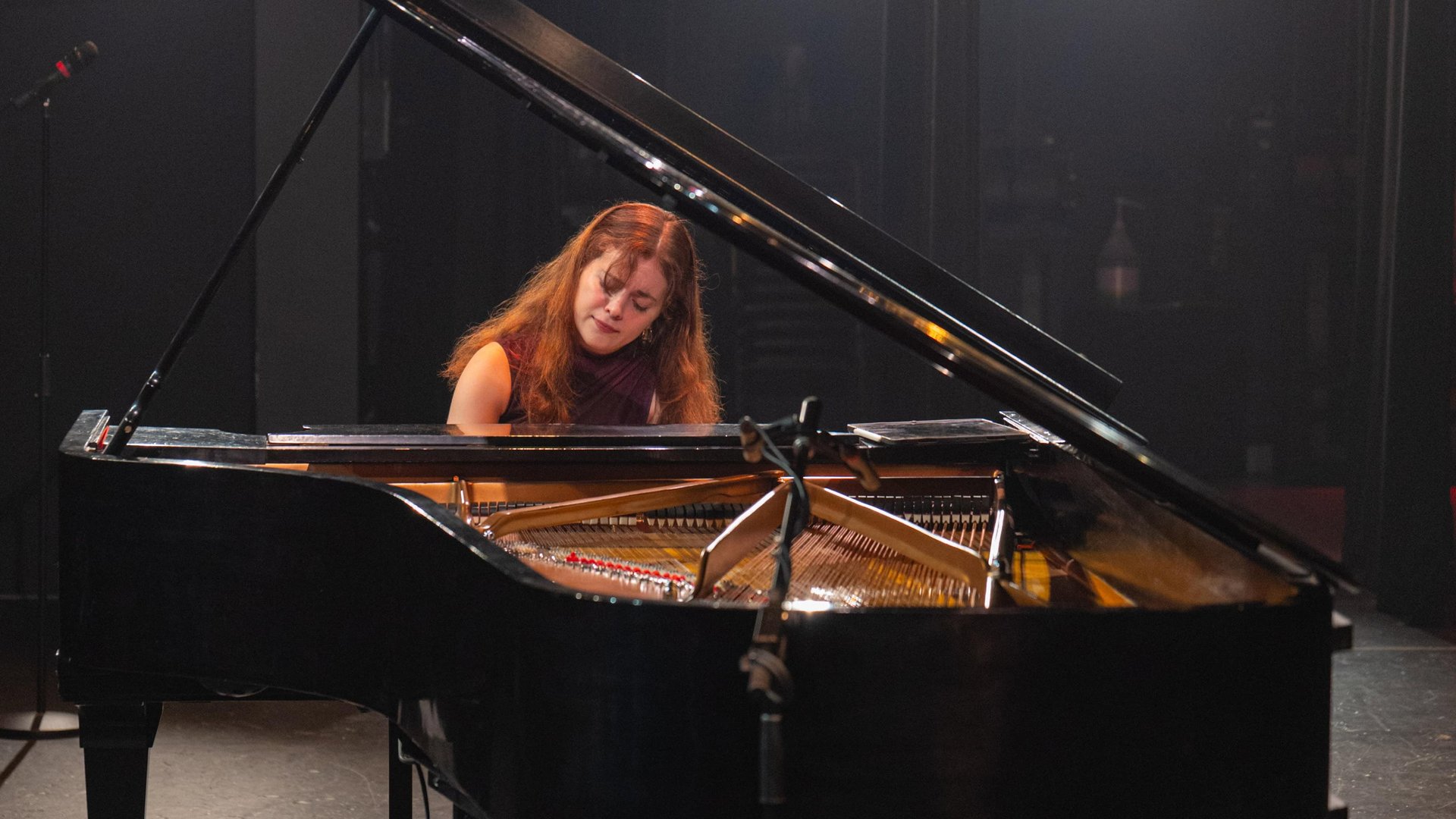 La pianiste Chloé Dumoulin joue sur un piano à queue au couvercle ouvert, sur une scène plongée dans le noir.