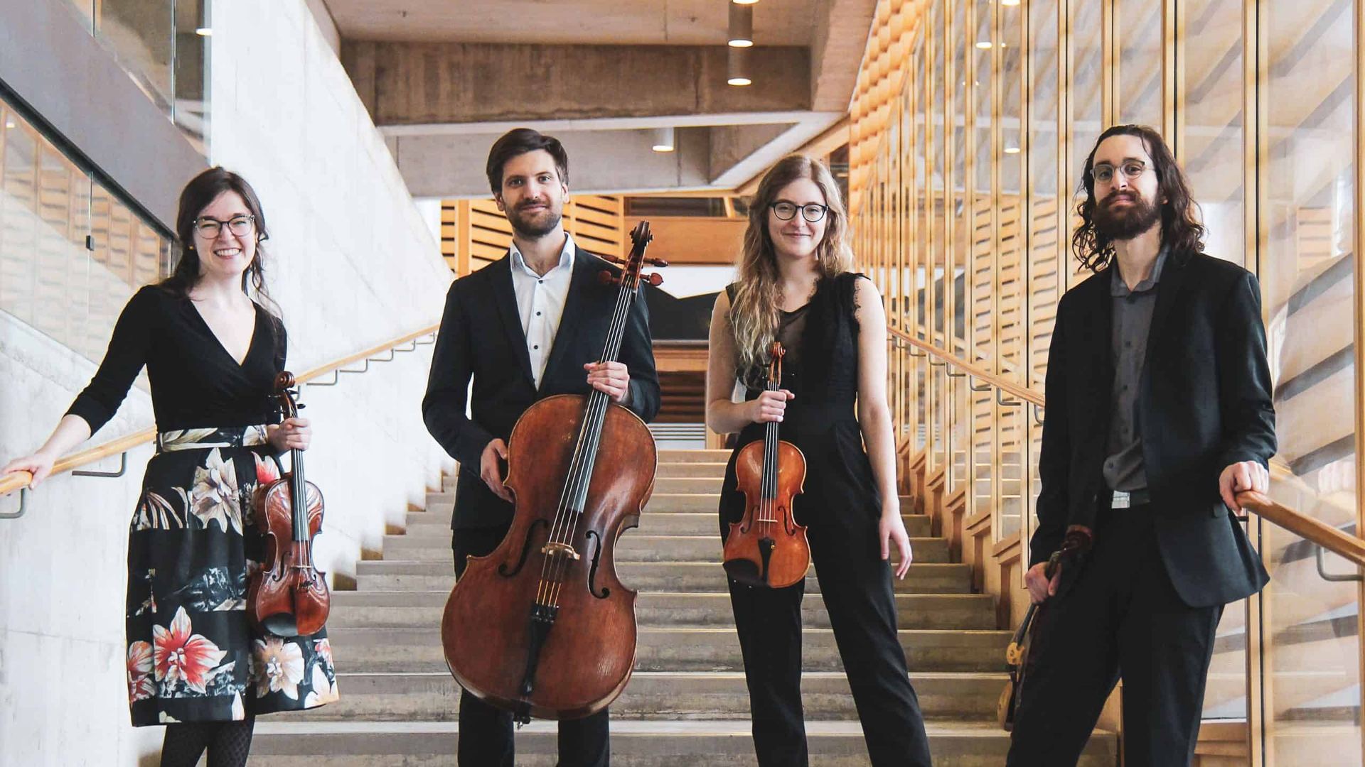Le Quatuor Andara, debout dans un escalier de bois clair, instruments à la main