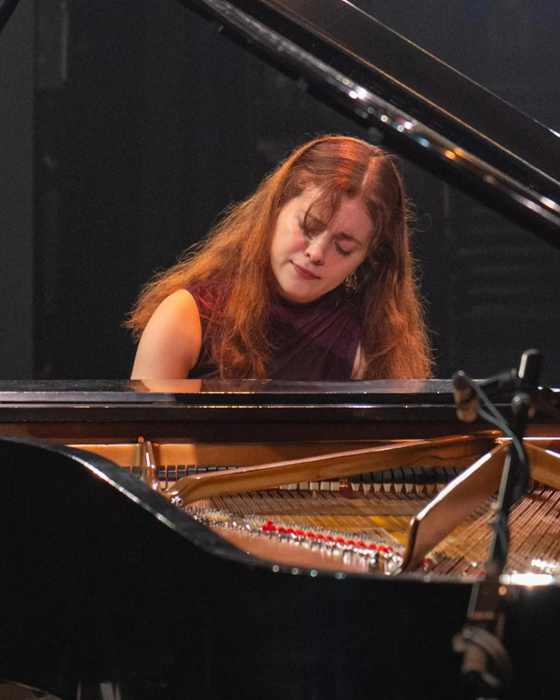 Chloé Dumoulin au piano à queue, sur une scène sombre.