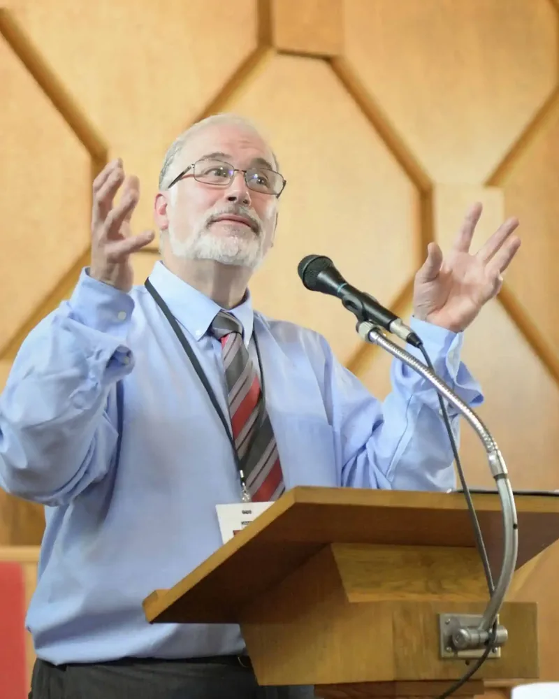 Richard Turp au lutrin, les mains levées, en pleine présentation