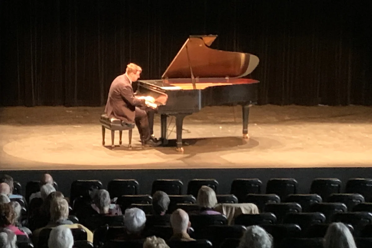 Un pianiste joue sur scène, vu du fond de la salle, derrière le public.
